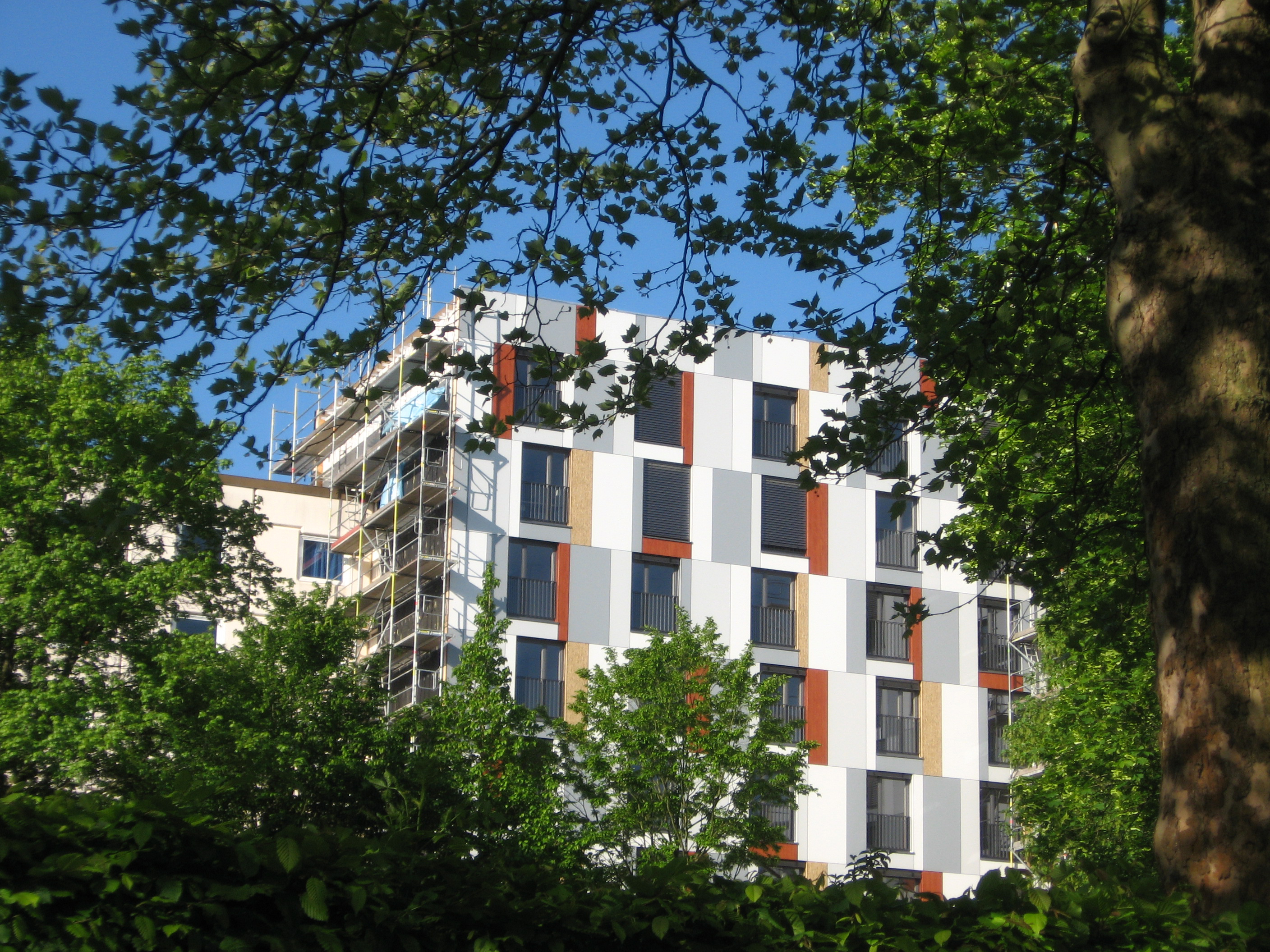 Bild von der Fassade des Studentenwohnheims in Bielefeld: größtenteils ist sie weiß, an den Fenstern gibt es jedoch rechteckige, rot-gelb-graue Elemente.
